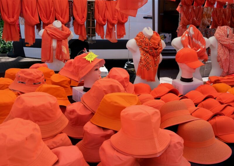 Orange hats and scarves are displayed for sale.